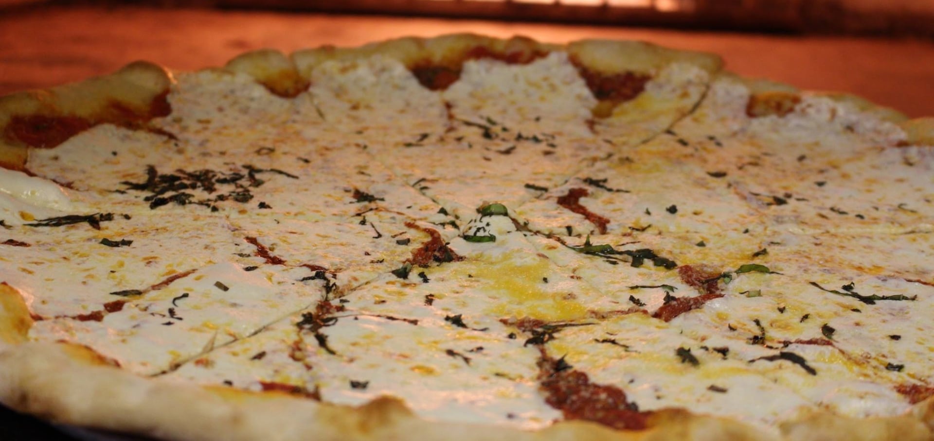 A close-up of a large cheese pizza with a golden-brown crust, melted mozzarella cheese, tomato sauce, and scattered bits of chopped basil—perfect from your favorite pizza restaurant in Bergen County NJ.